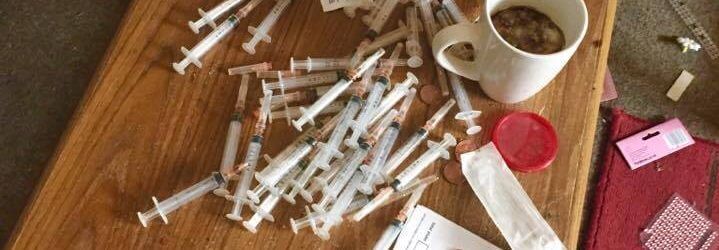 This is a picture of 25+ hypodermic syringes on a coffee table in a drug den. Ready to be removed with a specialist needle collection service